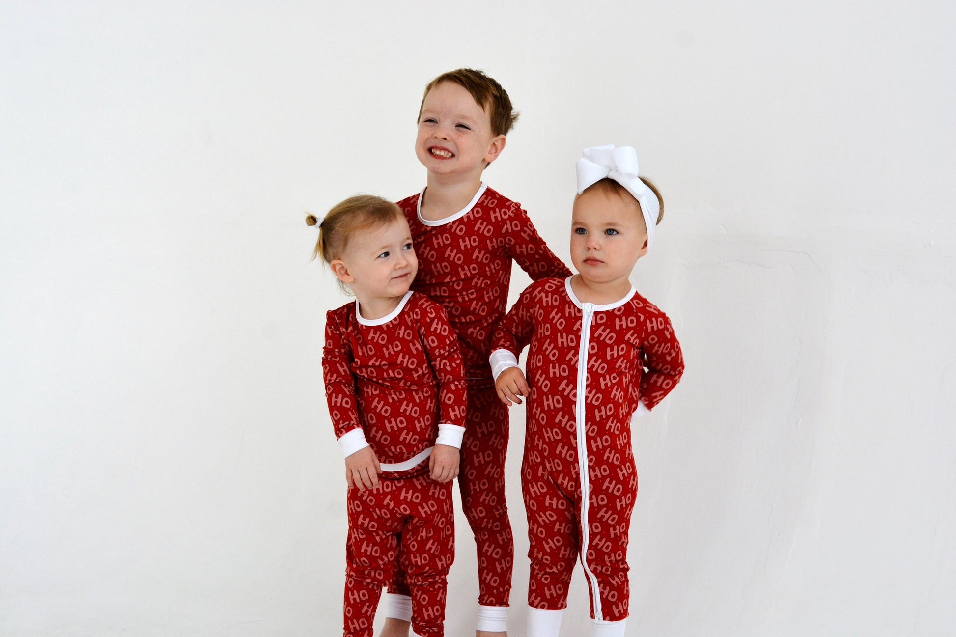 Three siblings in matching red Ho Ho Ho bamboo Christmas pajamas — family holiday sleepwear for babies and toddlers | AddieGrey & Co